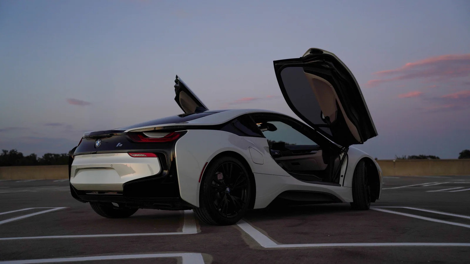 White BMW i8 with both butterfly doors open at dusk in Dallas